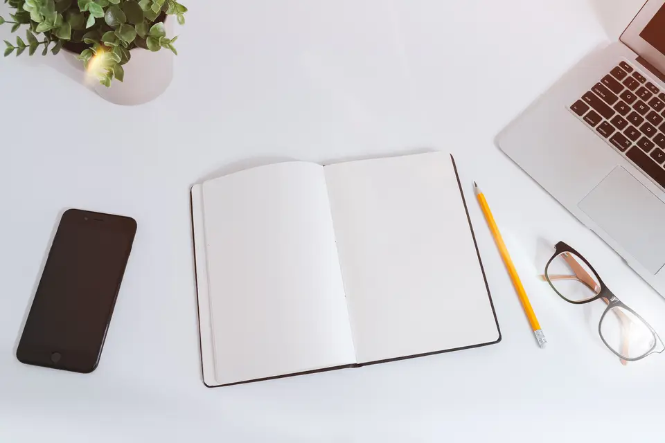 Beyaz çalışma masasında açık defter, kalem ve dizüstü bilgisayar